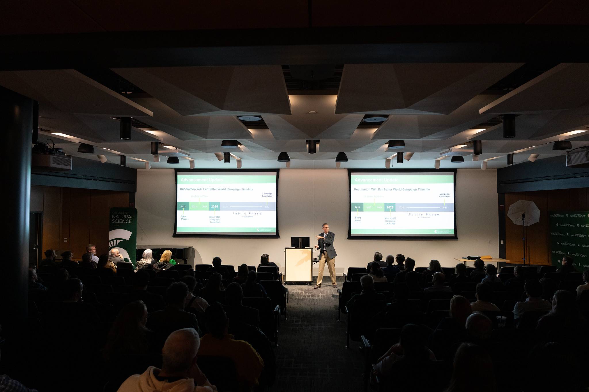 Dean Eric Hegg stands between projector screens, gesturing toward an audience.